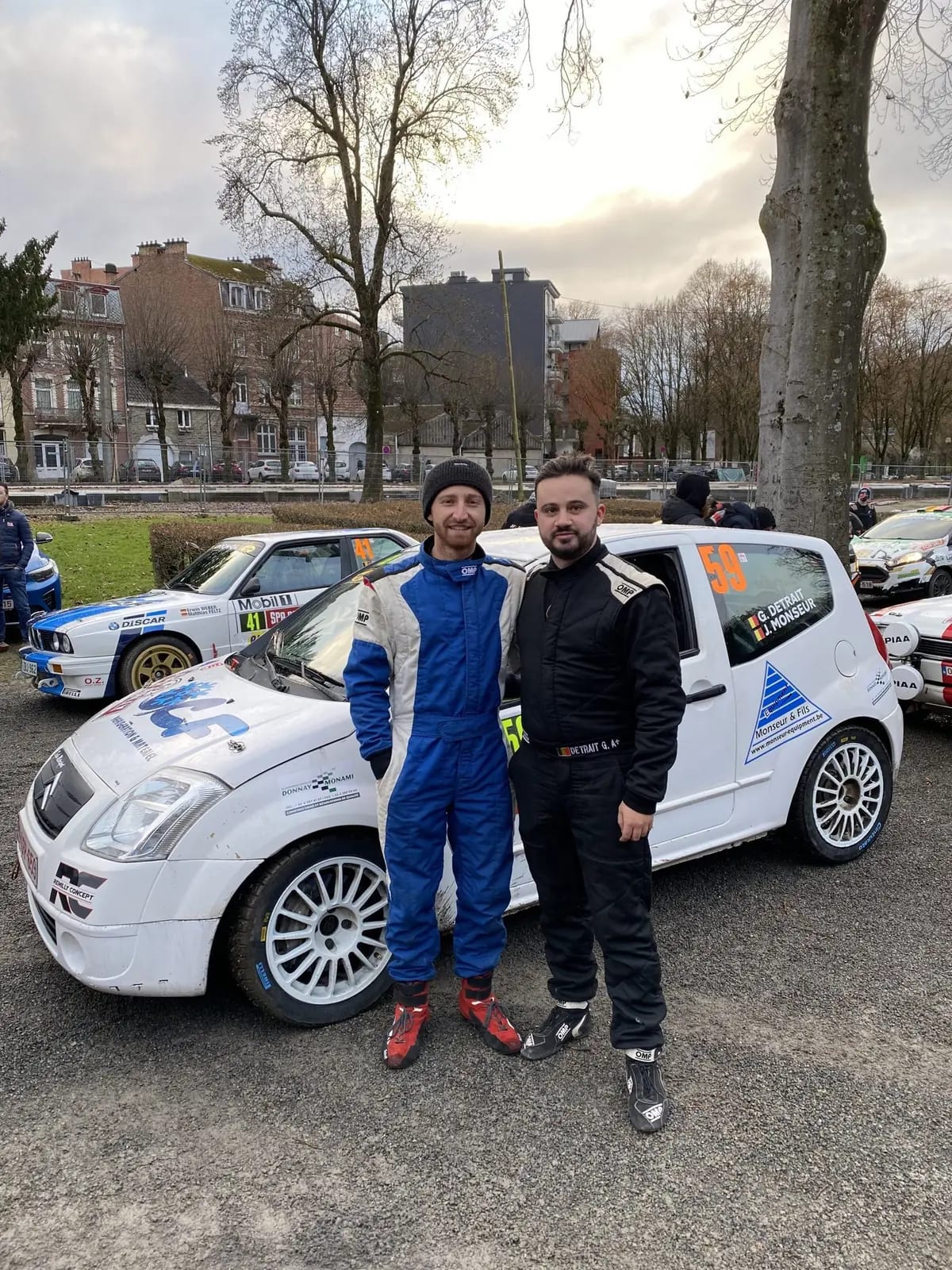 Jonathan Monseur en combinaison, devant sa voiture de course au parc fermé